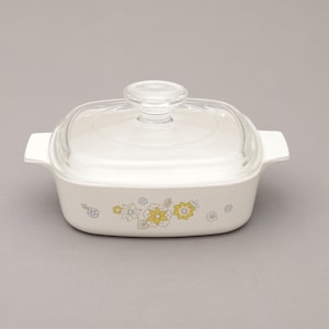 May include: White casserole dish with a clear glass lid. The dish has a rectangular shape with handles and is decorated with yellow and gray floral patterns. A classic piece of kitchenware.