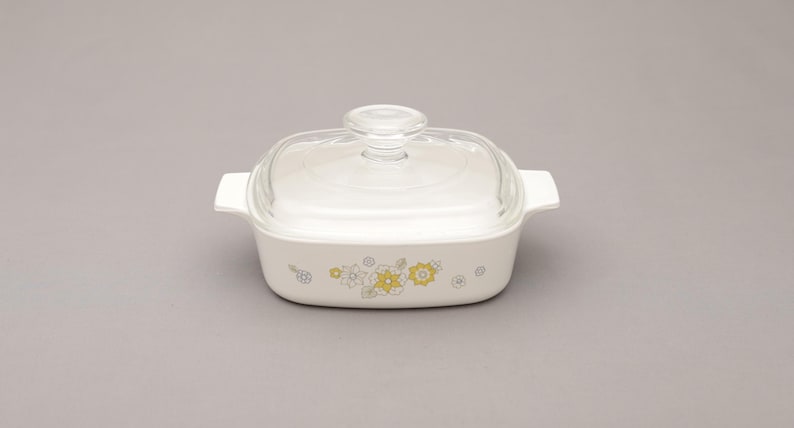 May include: White casserole dish with a clear glass lid. The dish has a rectangular shape with handles and is decorated with yellow and gray floral patterns. A classic piece of kitchenware.