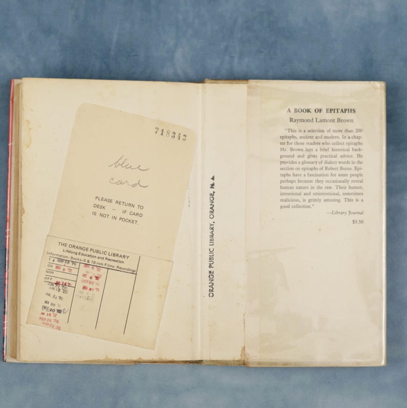 Puede incluir: Libro abierto titulado "A Book of Epitaphs" de Raymond Lamont Brown. Se inserta una tarjeta de biblioteca. El libro es de la Biblioteca P&uacute;blica de Orange. El libro est&aacute; abierto en la p&aacute;gina del t&iacute;tulo.