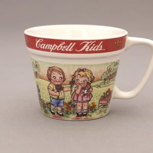 May include: White ceramic mug with a red band featuring the text "Campbell Kids." The mug has a handle and a colorful illustration of two children in a garden setting. The mug is a collectible item.