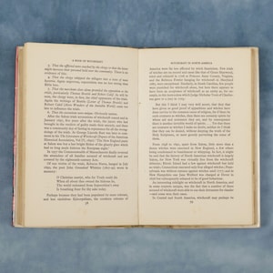Puede incluir: P&aacute;ginas de un libro abierto con texto sobre la brujer&iacute;a en Am&eacute;rica. El texto est&aacute; en fuente negra y se divide en dos columnas. La p&aacute;gina izquierda discute los juicios de brujas de Salem y la p&aacute;gina derecha la brujer&iacute;a en Am&eacute;rica del Norte. El libro est&aacute; abierto sobre una superficie de madera.
