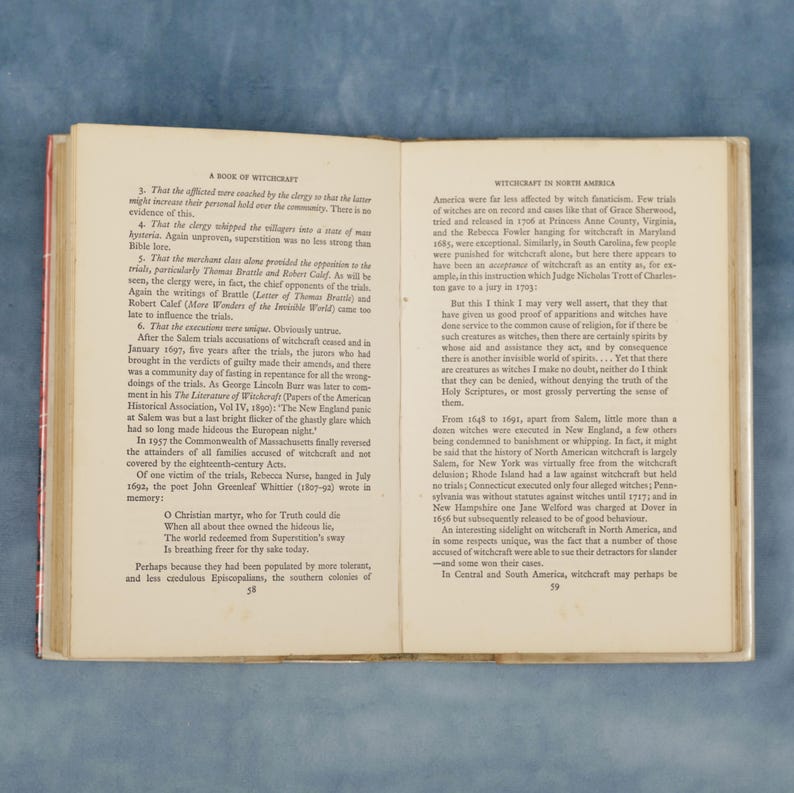 Puede incluir: P&aacute;ginas de un libro abierto con texto sobre la brujer&iacute;a en Am&eacute;rica. El texto est&aacute; en fuente negra y se divide en dos columnas. La p&aacute;gina izquierda discute los juicios de brujas de Salem y la p&aacute;gina derecha la brujer&iacute;a en Am&eacute;rica del Norte. El libro est&aacute; abierto sobre una superficie de madera.