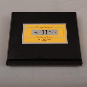 May include: A black rectangular box with a yellow and white label. The label reads "Vintage Series 2006" and "Aged 11 Years." Below the text is "San Andreas Wrapper" and "Rocky Patel."
