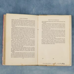 Puede incluir: Libro antiguo abierto con textos sobre brujer&iacute;a y superstici&oacute;n. La p&aacute;gina izquierda detalla creencias hist&oacute;ricas, la derecha pr&aacute;cticas relacionadas. Las p&aacute;ginas 98 y 99 son visibles, con un sello de la Biblioteca P&uacute;blica de Orange, Orange, MA.