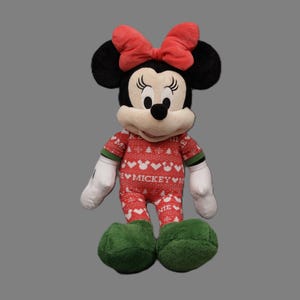 May include: A plush Minnie Mouse doll wearing a red and white patterned onesie with the word "Mickey" and green accents. She has black ears, a red bow, white gloves, and green shoes. The doll is standing upright.
