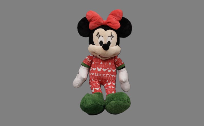 May include: A plush Minnie Mouse doll wearing a red and white patterned onesie with the word "Mickey" and green accents. She has black ears, a red bow, white gloves, and green shoes. The doll is standing upright.