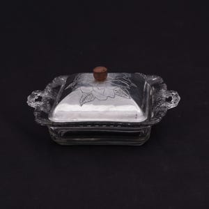 May include: A clear glass butter dish with a silver lid featuring a floral design. The lid has a wooden knob.