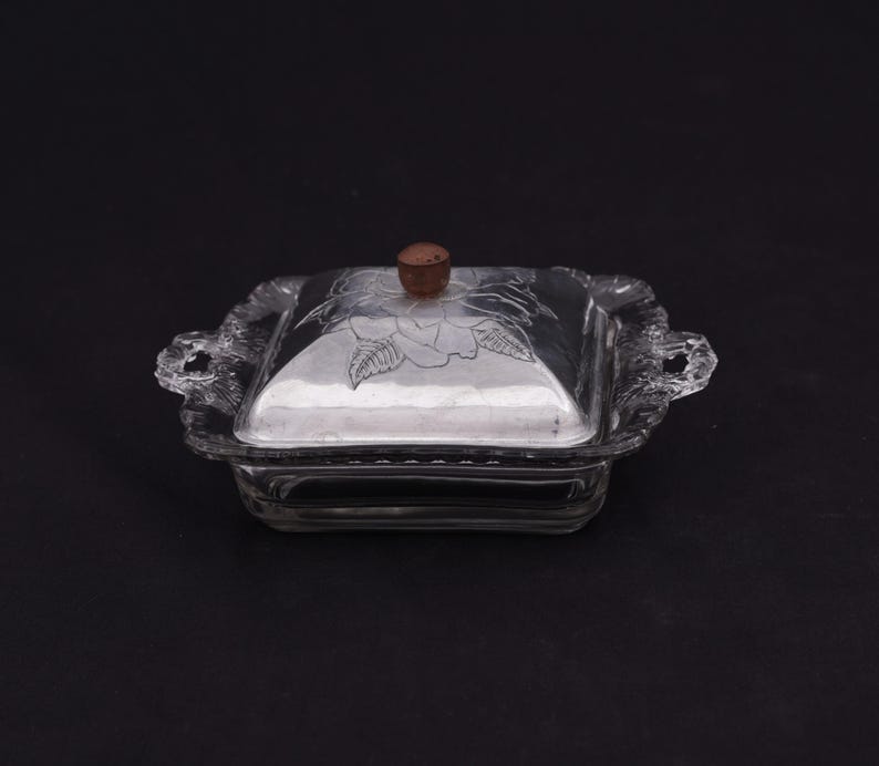 May include: A clear glass butter dish with a silver lid featuring a floral design. The lid has a wooden knob.