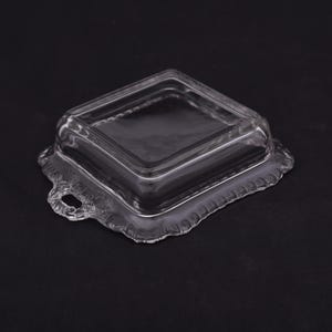 May include: A clear glass square dish with a lid. The dish has a decorative scalloped edge and a handle on each side.