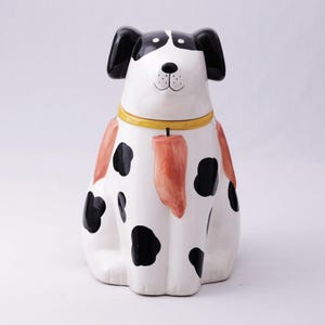 May include: A ceramic dog figurine with a white base, black spots, and black ears. The dog has a yellow collar and orange markings. The figurine is a decorative item, likely for home decor.