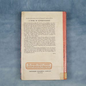 Puede incluir: Contraportada de un libro antiguo, "A Book of Superstitions" de Raymond Lamont Brown. La cubierta es blanquecina con texto negro, que detalla el contenido del libro. Incluye el logotipo de la Biblioteca P&uacute;blica de Orange y la informaci&oacute;n del editor.