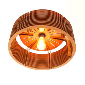 Puede incluir: Una l&aacute;mpara colgante de madera con una luz c&aacute;lida y acogedora. El dise&ntilde;o circular presenta listones de madera en capas y una bombilla central. La l&aacute;mpara est&aacute; suspendida del techo, mostrando su dise&ntilde;o &uacute;nico y moderno.