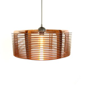 Puede incluir: Una moderna l&aacute;mpara colgante con un brillo c&aacute;lido y acogedor. La l&aacute;mpara presenta una pantalla circular de madera con listones horizontales, suspendida de un cable fino. La bombilla expuesta es visible, creando un ambiente acogedor. El accesorio est&aacute; sobre un fondo blanco.