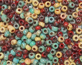 Puede incluir: Una colección de pequeñas cuentas de vidrio redondas en varios colores, incluyendo crema, turquesa y rojo. Las cuentas tienen un aspecto moteado o jaspeado.