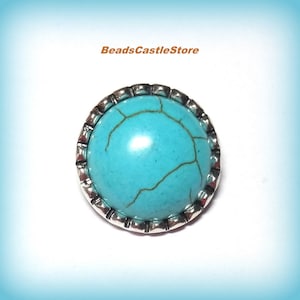 May include: A round turquoise cabochon set in a silver-colored bezel. The turquoise stone has brown veining. The bezel has a decorative, square-edged design. The text "BeadsCastleStore" is in the upper left corner.