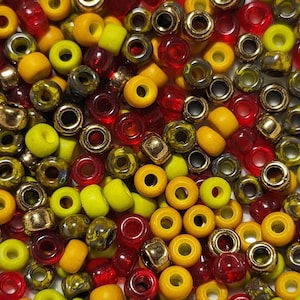 May include: A close-up image of a variety of small, round beads in shades of yellow, red, and gold. The beads are made of glass and have a smooth, shiny finish.