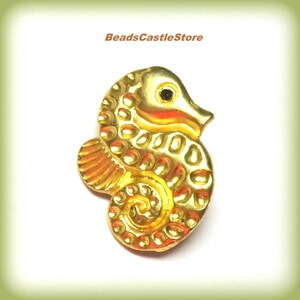 May include: Gold-colored metal seahorse charm with a black eye. The seahorse has a textured surface and a curled tail.
