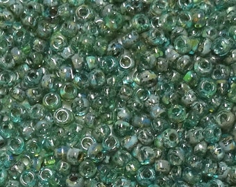 May include: A close-up of a large quantity of small, round, green glass beads with iridescent shimmer. The beads have a slightly irregular shape and a hole in the center.