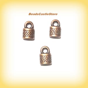 May include: Three antique copper-colored metal cord end caps with a decorative design. Each cap has a small loop at the top.