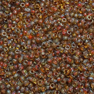 May include: A close-up image of a large quantity of small, round, glass beads. The beads are a mix of amber, brown, and red colors with white speckles.