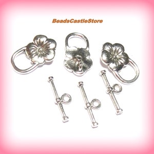May include: Silver tone flower toggle clasps with matching silver tone toggle bars. The flower clasps have a raised center design.