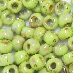 May include: A collection of small, round, light green glass beads with a white and brown marbled pattern. The beads have a hole in the center for stringing.