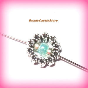 May include: A silver flower bead with a light blue and white bead in the center. The bead is on a silver wire.
