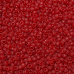 May include: A close-up view of a pile of small, round, red beads. The beads are densely packed together, filling the frame. Each bead has a small hole running through the center. The beads have a matte finish.