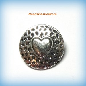 May include: Silver charm with a hammered texture and a raised heart in the center.