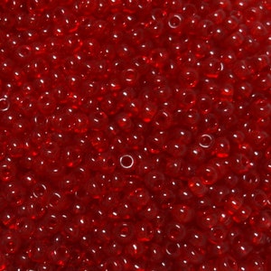 May include: A close-up image of a large quantity of small, round, red beads. The beads are translucent and have a slight shine.