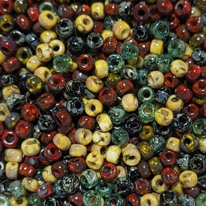 May include: A collection of small, round, glass beads in various colors, including black, white, red, green, and yellow. The beads have a speckled or marbled appearance.
