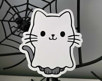 May include: A white ghost cat sticker with black eyes and a black nose. The sticker is on a black spider web background.