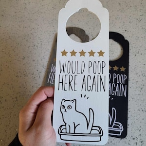 Peut inclure: Porte-manteau blanc avec une illustration noir et blanc d'un chat dans une litière. Le porte-manteau a une note de cinq étoiles et le texte "Would poop here again".