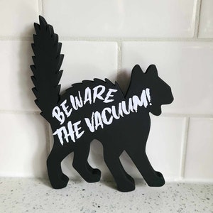 May include: Black silhouette of a cat with a white warning sign that reads "Beware the Vacuum!"