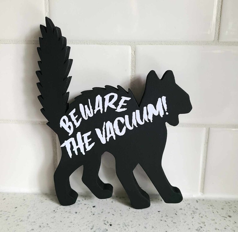 May include: Black silhouette of a cat with a white warning sign that reads "Beware the Vacuum!"