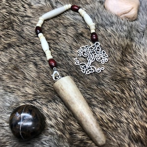 May include: A white and brown bone pendant with a silver Celtic knot tree of life charm hanging from a white and brown beaded necklace.