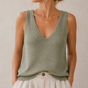 Puede incluir: Una camiseta de tirantes de punto en color verde salvia con un escote en V profundo, tirantes anchos con textura acanalada y un dobladillo acanalado a juego. La prenda está confeccionada con un patrón de punto vertical y pantalones beige.