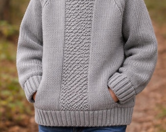 Può includere: Una felpa con cappuccio a maniche lunghe color grigio chiaro caratterizzata da un motivo a maglia testurizzato sul davanti, polsini a coste, orlo a coste e due tasche frontali. Il capo è indossato con un paio di jeans blu.
