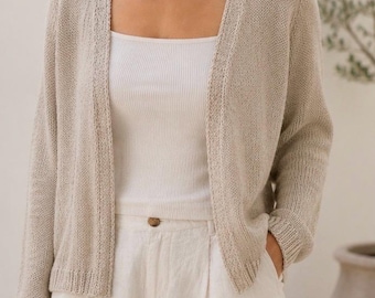 Può includere: Un cardigan in maglia beige aperto sul davanti con maniche lunghe e polsini a coste, indossato sopra una canotta bianca a coste e pantaloni chiari con un unico bottone visibile in vita. Il cardigan presenta una trama in maglia fine e leggera.
