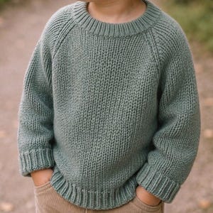 Peut inclure: Un pull en tricot à manches longues vert sauge doté d'un col rond côtelé, de poignets côtelés et d'un ourlet côtelé. Le vêtement est construit avec un motif en tricot vertical et des manches raglan, offrant un aspect texturé sur toute la pièce.