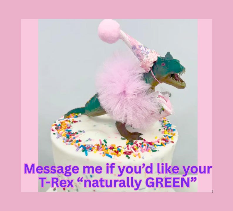 May include: A green T-Rex dinosaur figurine wearing a pink tulle tutu and a matching pink party hat with a pom-pom, standing on a white cake decorated with colorful sprinkles. The text reads: Message me if you'd like your T-Rex naturally GREEN.