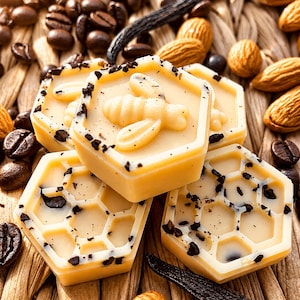 May include: Close-up of several hexagonal, pale yellow soaps with a bee design and dark flecks. The soaps are surrounded by coffee beans, almonds, and a vanilla pod. The soaps have a honeycomb pattern.