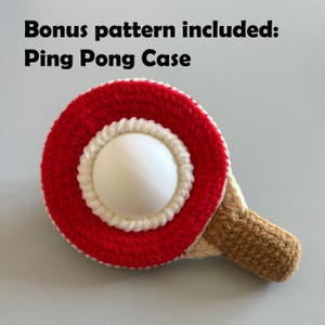 May include: A crocheted ping pong paddle with a red and white circular design and a brown handle. The text "Bonus pattern included: Ping Pong Case" is at the top of the image.