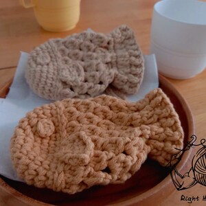May include: Two crocheted tan and brown  fish-shaped  coasters on a wooden surface. The coasters are made with a textured stitch pattern.