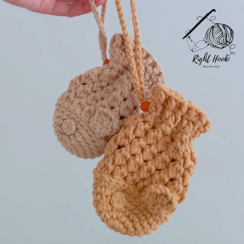 May include: Two crocheted fish-shaped pouches with orange beads. The pouches are beige and light brown. The pouches are hanging from a string.