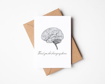 May include: A white card with a black and white illustration of a brain. The text on the card reads "Thank you for fixing my brain."