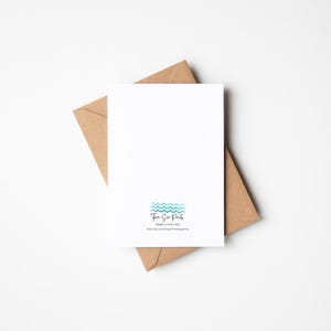 May include: A blank white greeting card with a blue and green wave design and the text "Three Sea Prints" and "Made in the USA" on the back. The card is sitting on a brown envelope.