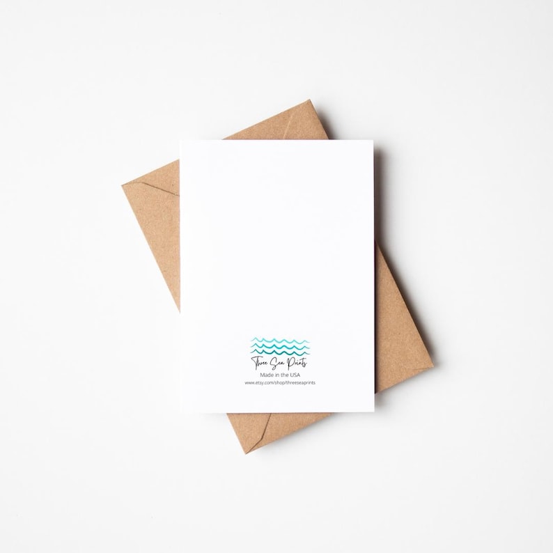 May include: A blank white greeting card with a blue and green wave design and the text "Three Sea Prints" and "Made in the USA" on the back. The card is sitting on a brown envelope.