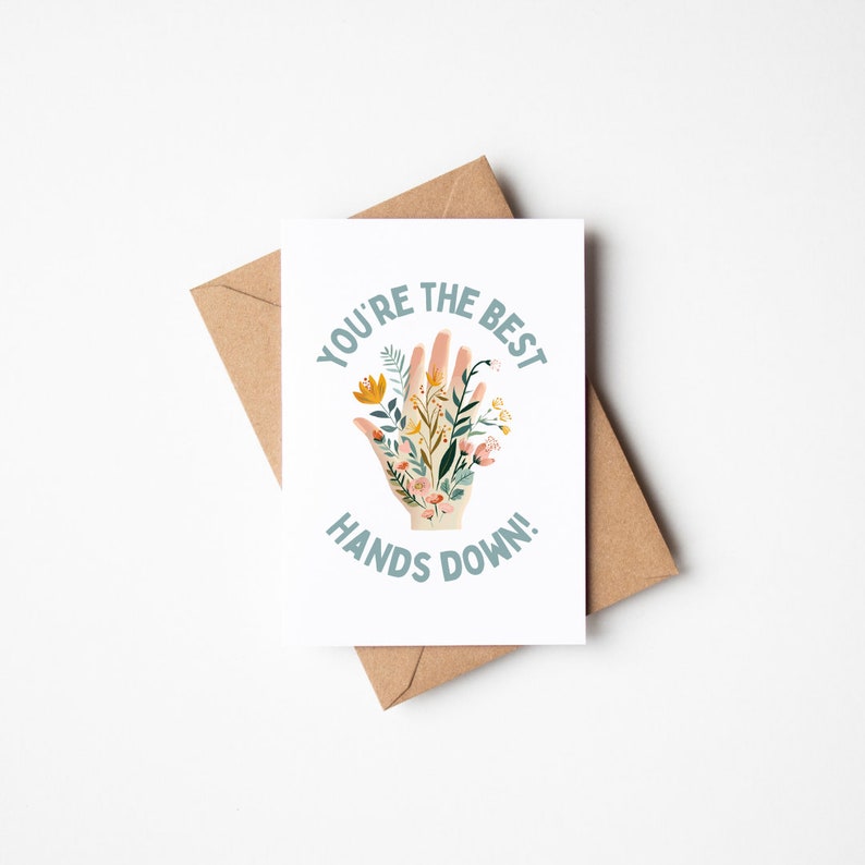 May include: A white card with a hand-drawn illustration of a hand with flowers growing out of it. The text "You're the best hands down!" is written in a teal blue font around the hand.
