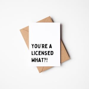 Op de afbeelding: Een witte wenskaart met de tekst "YOU'RE A LICENSED WHAT?!" in het zwart, op een bruine envelop. De kaart en envelop liggen op een witte achtergrond. De kaart heeft een standaard rechthoekige vorm.